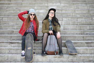 A young hipster girl is riding a skateboard. Girls girlfriends for a walk in the city with a skateboard. Spring sports on the street with a skateboard.