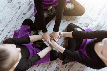 Top view of kids in black uniform and skirt sitting on floor at dance studio after dancing modern ballet, embracing and smiling together in the class.