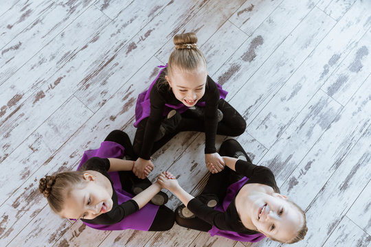 Top View Of Kids In Black Uniform And Skirt Sitting On Floor At Dance Studio After Dancing Modern Ballet, Embracing And Smiling Together In The Class.