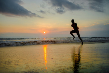 silhouette of young attractive fit athletic and strong black afro American man running at sunset beach training hard and sprinting on sea water runner workout