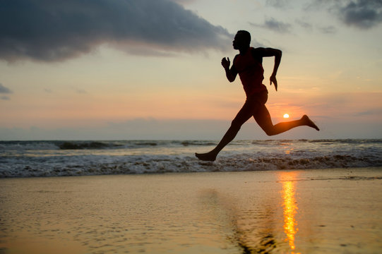 silhouette of young attractive fit athletic and strong black African American man running at sunset beach training hard and sprinting on sea water runner workout