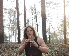 A musician with a tool in nature. A man is playing a flute in a pine forest. The music of the druids in the spring forest.