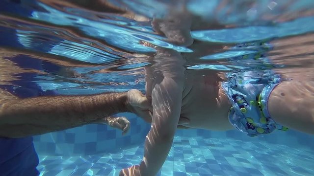 Happy smiling toddler is diving under water with father
