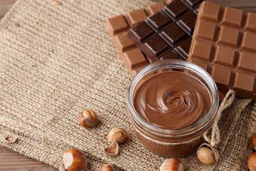 Chocolate spread or nougat cream with hazelnuts in glass jar on sack cloth background