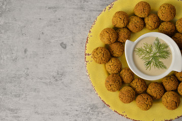 Baked chickpea falafel balls on yellow plate on grey background , healthy and vegan food with tahini deep , traditional Mediterranean , top view , flat lay with copy space  