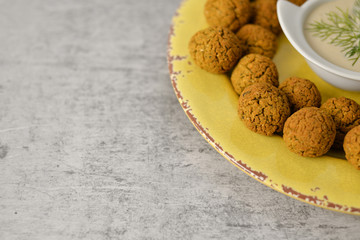 Baked chickpea falafel balls on yellow plate on grey background , healthy and vegan food with tahini deep , traditional Mediterranean , top view , flat lay with copy space  