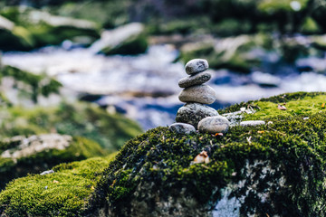 Fototapeta na wymiar Balancing rock art. Stones balanced on top of each other on the stone with moss. Green color, flowing creek and a stone man. Zen stones or zen stack in the forest next to a river.