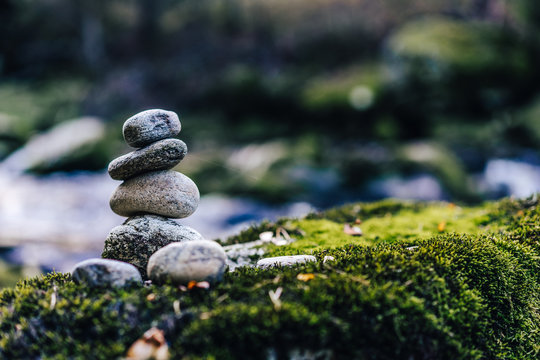 Balancing rock art. Stones balanced on top of each other on the stone with moss. Green color, flowing creek and a stone man. Zen stones or zen stack in the forest next to a river.
