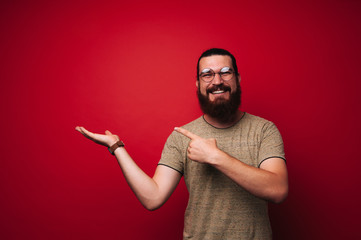 Portrait of smiling bearded boy, pointing to copy space, over red background