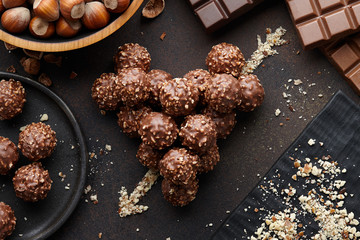 Heart shape with arrow made from chocolate truffle candies with hazelnuts and nut crumb on brown textured background, top view