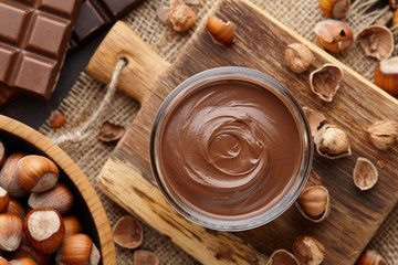 Chocolate spread or nougat cream with hazelnuts in glass jar, bowl of nuts and chocolate bars on...