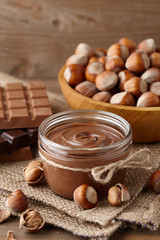 Chocolate spread or nougat cream with hazelnuts in glass jar on wooden background