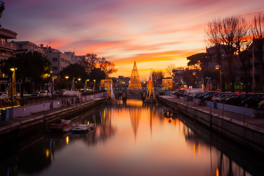 View of the Christmas Tree on a bridge at sunset, with orange clouds. Long exposure picture in Riccione, Emilia Romagna, Italy.