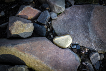 A pile of Gold nugget grains, on big river stone. Golden texture.