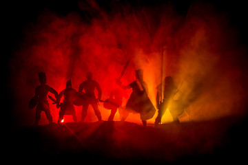 Fototapeta premium Medieval battle scene. Silhouettes of figures as separate objects, fight between warriors on dark toned foggy background. Night scene.