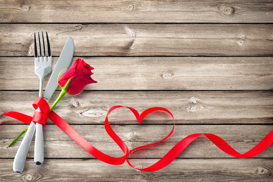 Silverware tied up with red ribbon in heart shape on wooden planks