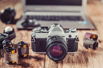 Analog camera, film rolls and vintage photography accessories along with modern equipment and laptop.