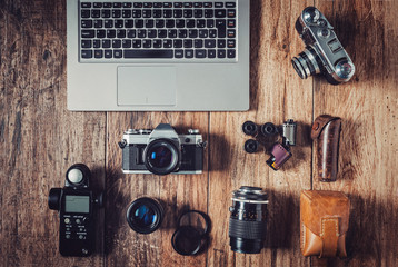 Analog camera, film rolls and vintage photography accessories along with modern equipment and laptop.