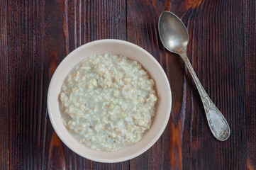 Tasty sweet oatmeal in a bowl on wooden table. Top view.