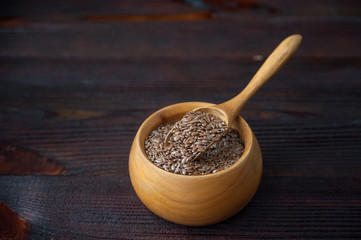 Brown flax seeds in wooden bowl and spoon on table.