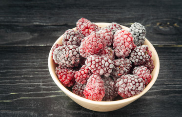 Frozen blackberries in a bowl on a wooden dark background.