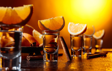 Glasses of tequila with orange and cinnamon sticks.