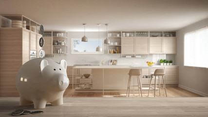Wooden table top or shelf with white piggy bank with coins, modern white and wooden kitchen,...