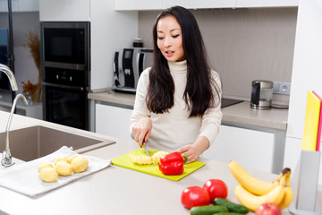 Image of happy brunette cutting potatoes at table with vegetables and fruits