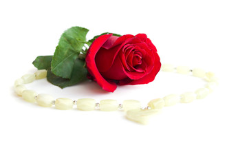 Beads with a pendant in the shape of a heart around a red rose on a white background