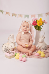 Cute funny baby with bunny ears and colorful Easter eggs and rabbits. Easter Baby. Greeting Easter card template. Girl baby in suit of rabbit for Easter. 