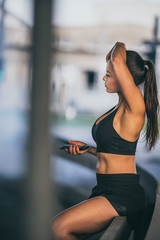 Beautiful Confident Fitness Girl in Black Athletic Top is Using a Smartphone on a Street. She is in an Urban Environment Under a Bridge with Cars in the Background.