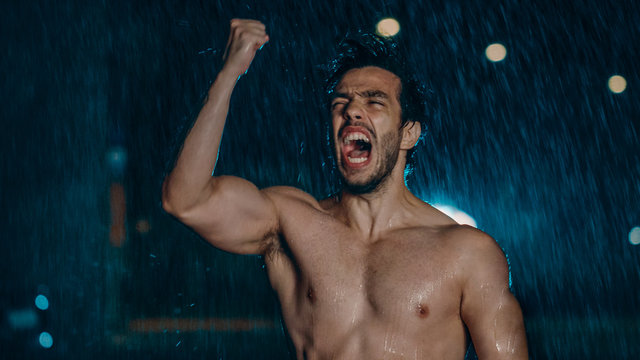 Shirtless Athletic Muscular Young Man is Celebrating His Sport Accomplishments on a Rainy Night. He is in an Urban Environment Under a bridge with Cars in the Background.