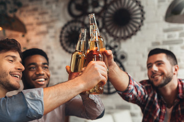 Guys clinking bottles of beer, resting in bar