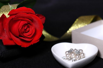 赤い薔薇の花と真珠のアクセサリーとプレゼントの箱と金色のリボン(黒背景)
