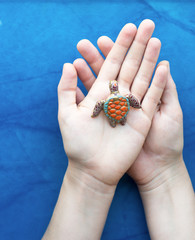 Artist hands palm up with handmade polymer clay jewelry brooch with sea tortoise on blue background