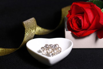 赤い薔薇の花と真珠のアクセサリーと金色のリボン(黒背景)