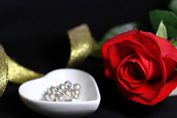 赤い薔薇の花と真珠のアクセサリーと金色のリボン(黒背景)