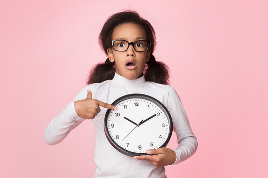 Surprised african-american girl holding big clock and pointing on it