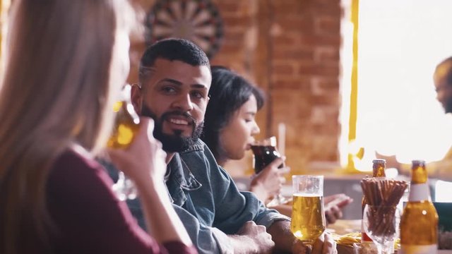 Young Arabian man talking with Caucasian girl near bar counter inside pub