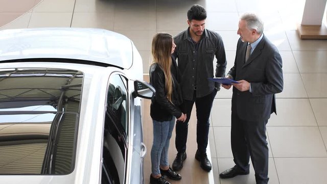 Car dealer exaplining a car's features to a couple by reading a document