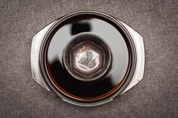 an empty glass in a bowl filled with dark liquid on a gray background