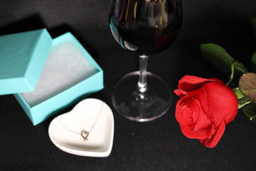 赤い薔薇の花とハートのネックレスとプレゼントの箱と赤ワインのグラス(黒背景)	