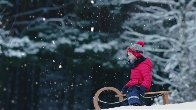 CINEMAGRAPH - SEAMLESS LOOP. Cute little kid boy child preparing for a sledge ride down the hill. Child plays outdoors in snow, winter fun. 4K UHD
