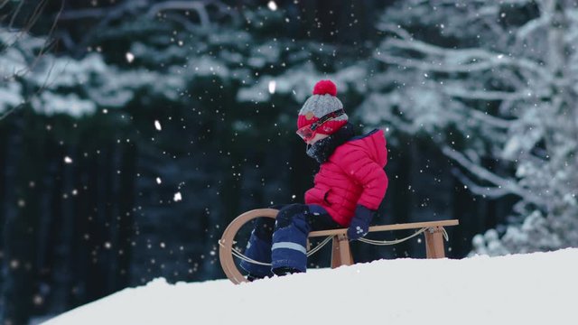 CINEMAGRAPH - SEAMLESS LOOP. Cute little kid boy child preparing for a sledge ride down the hill. Child plays outdoors in snow, winter fun. 4K UHD