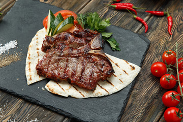 Grilled beef steak with rosemary, salt and pepper on black stone plate. Grilled striploin sliced steak. Juicy thick grilled beef steak seasoned with rosemary fresh of the summer BBQ.