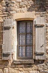 Old French window including shutters with old-fashioned curtains with birds motive hanging in a bricked medieval façade.