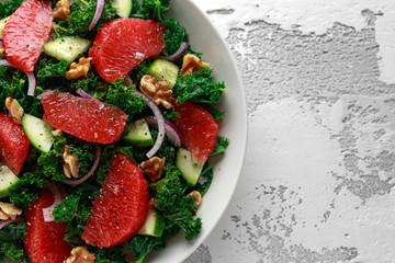 Healthy vegan, vegetarian Grapefruit kale salad with walnuts, red onion and cucumber on white...