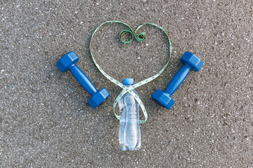 Green measure tape in heart form, water bottle and two dumbbells