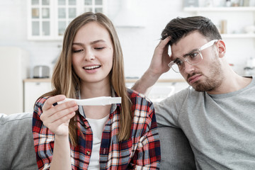 Photo of woman happy with positive ovulation test while man is upset and bewildered, not wanting to be father