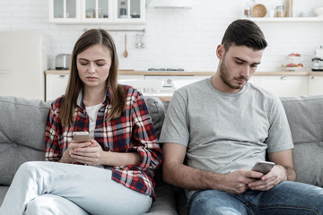 Young couple showing disinterest in each other after quarrel, each one using their cellphone